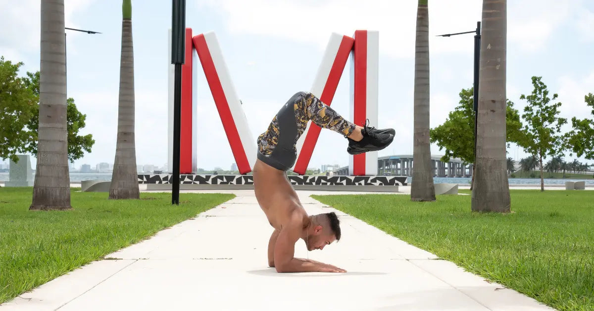 Athletic yoga leggings for men worn during an arm balance pose in a tropical outdoor setting.