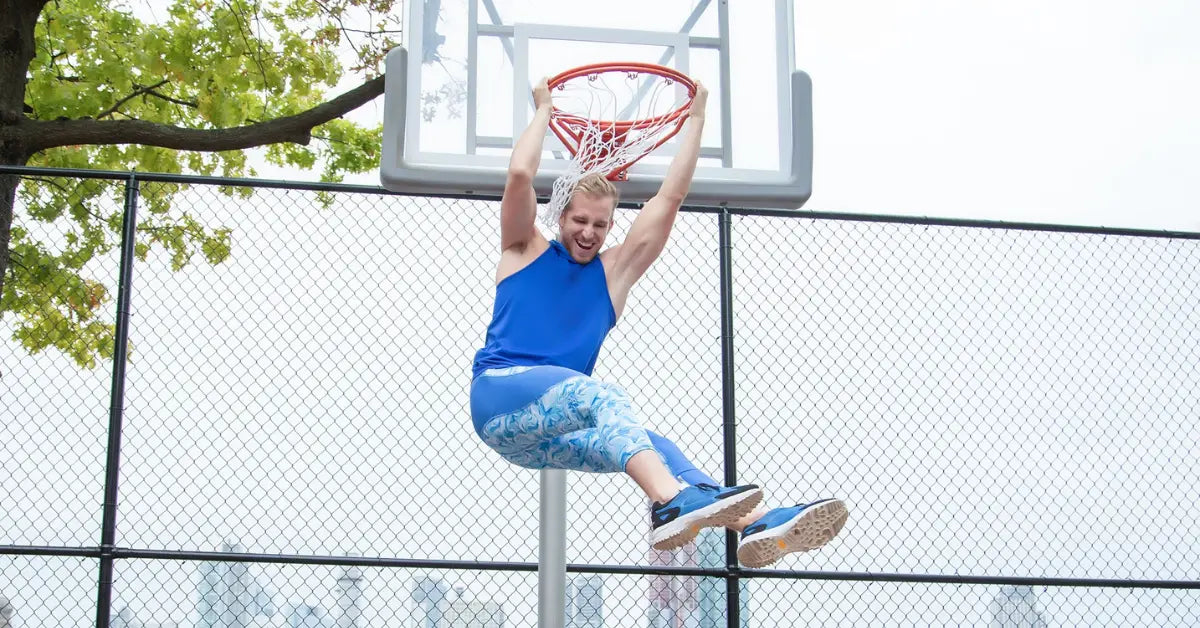 Athletic leggings for men in blue marble print worn by a man dunking on a basketball hoop outdoors