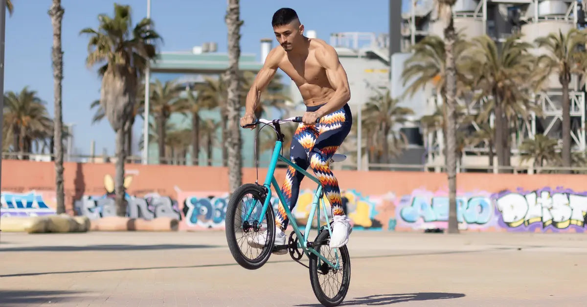 Men's cycling tights in a bold geometric print worn by a shirtless man performing a trick on a bike.
