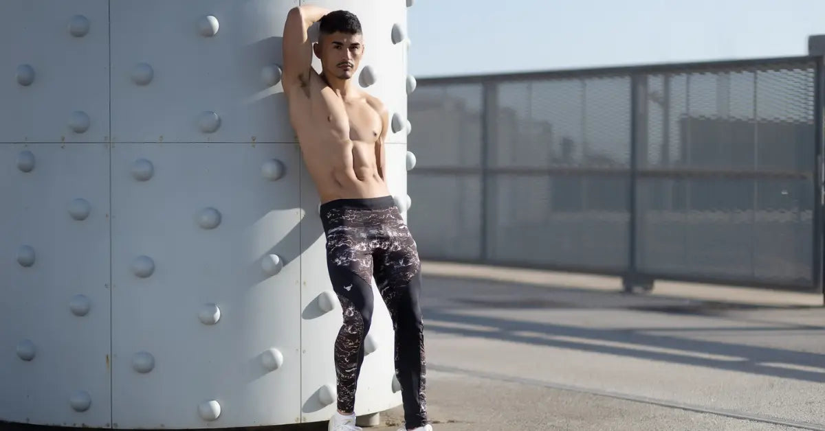 Modern men’s activewear with dark patterned leggings, worn by a man leaning against an industrial structure outdoors