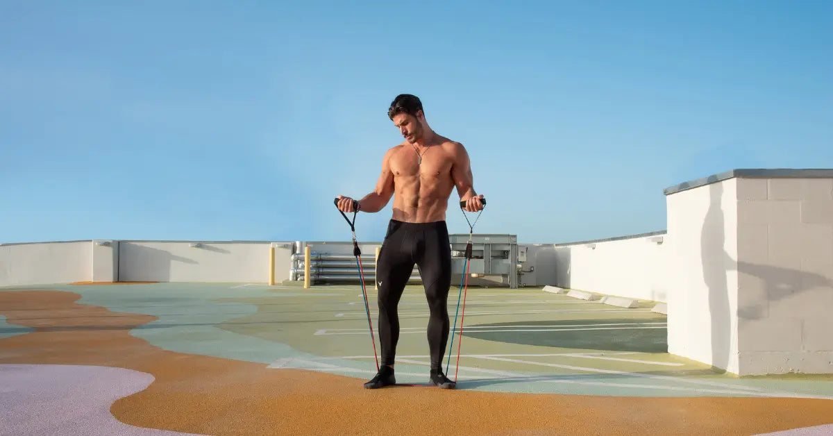 Running leggings for men in solid black worn by a shirtless man exercising with resistance bands on a rooftop